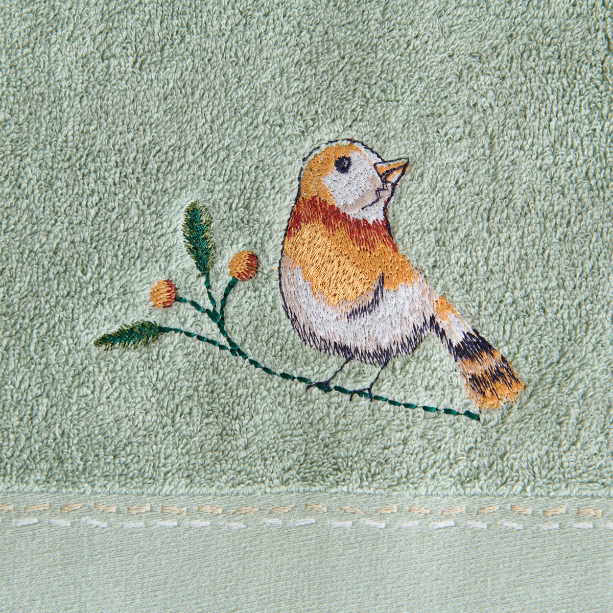Détail de la broderie d'oiseau sur une branche de la serviette Doux Refuge coloris Céladon, en éponge 600 g/m².