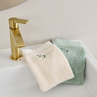 Gants de toilette Doux Refuge en éponge brodée 600 g/m², coloris Lin et Céladon, présentés dans une salle de bain.