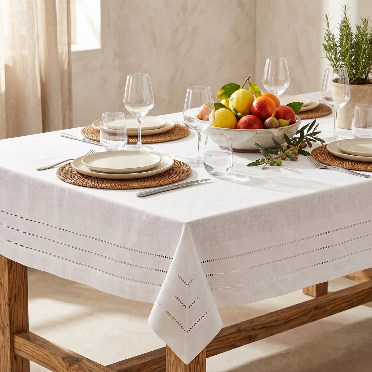 Nappe Jour Venise blanche en polyester, avec délicates lignes ajourées, présentée sur une table élégamment dressée avec vaisselle et fruits.