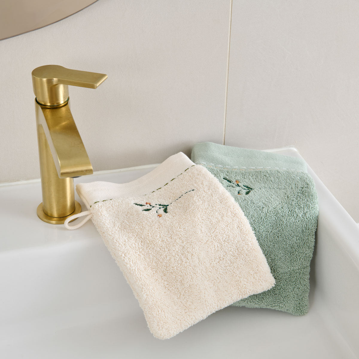 Gants de toilette Doux Refuge en éponge brodée 600 g/m², coloris Lin et Céladon, présentés dans une salle de bain.