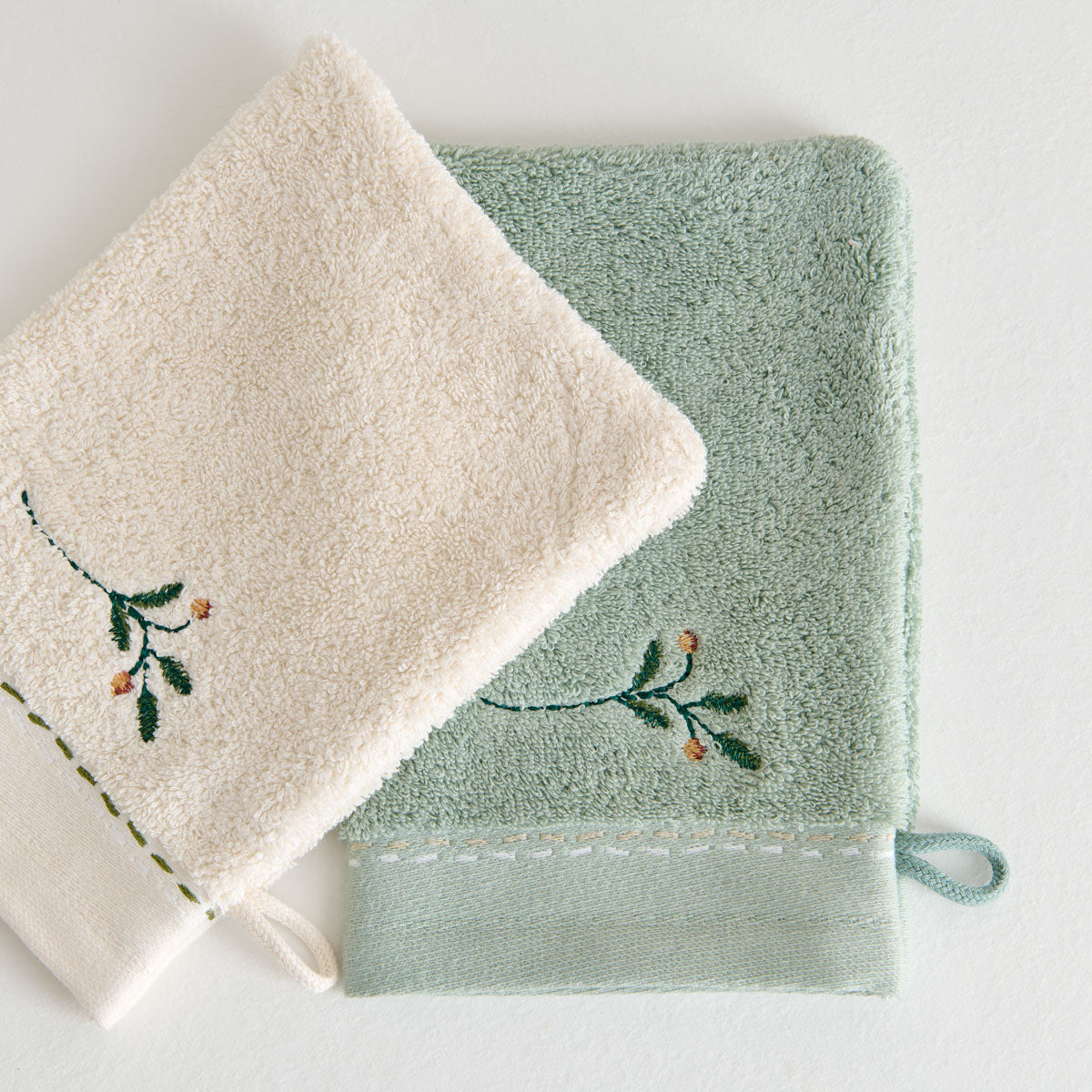 Gants de toilette Doux Refuge 16 × 21 cm, broderie végétale et finition mini-liteau, coloris Lin et Céladon.