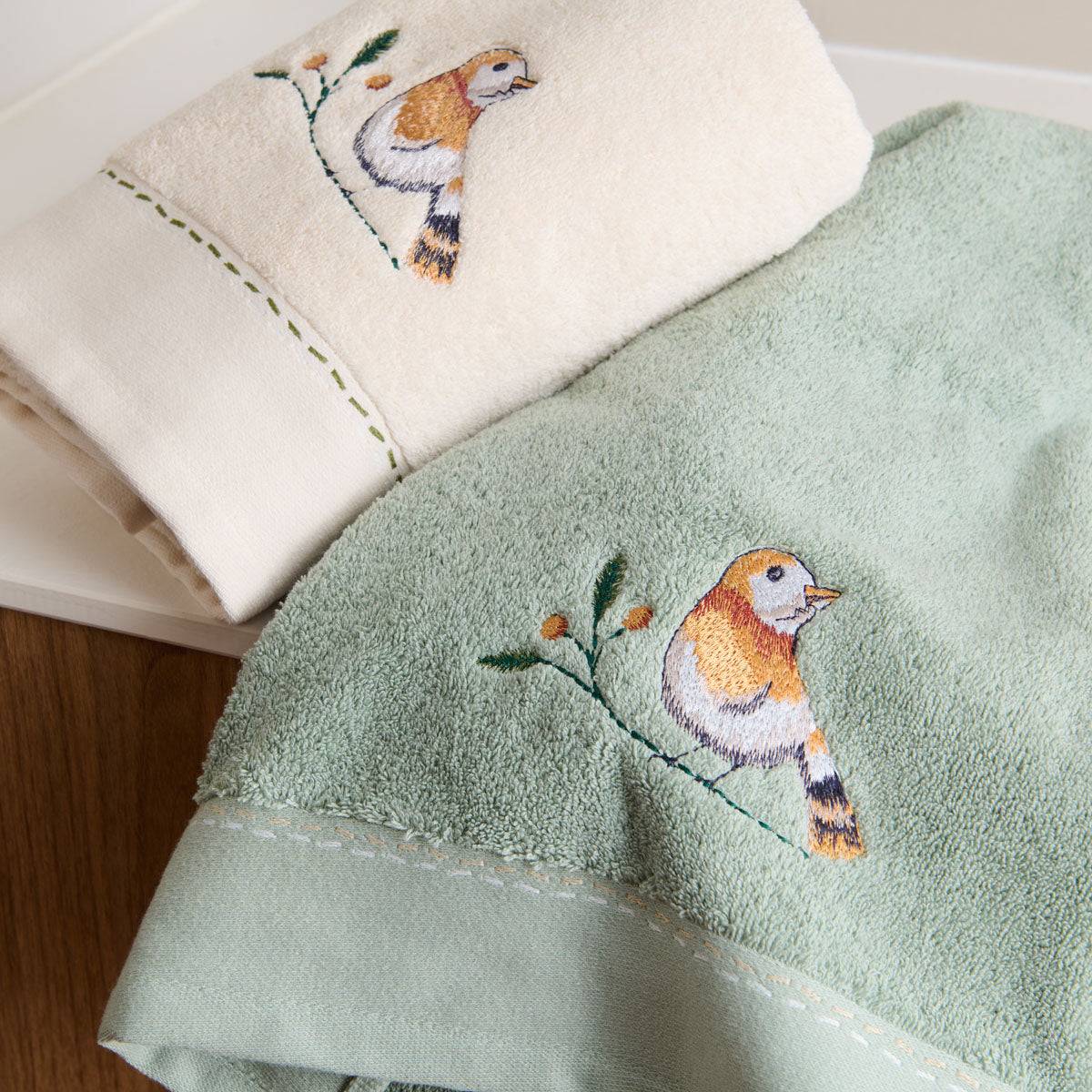 Détail des serviettes invitées Doux Refuge en coloris Lin et Céladon, avec broderie d'oiseau sur une branche et finition mini-liteau.