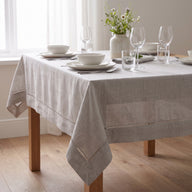 Nappe Florence en polyester texturé avec finition ajourée sur une table dressée avec vaisselle blanche et fleurs