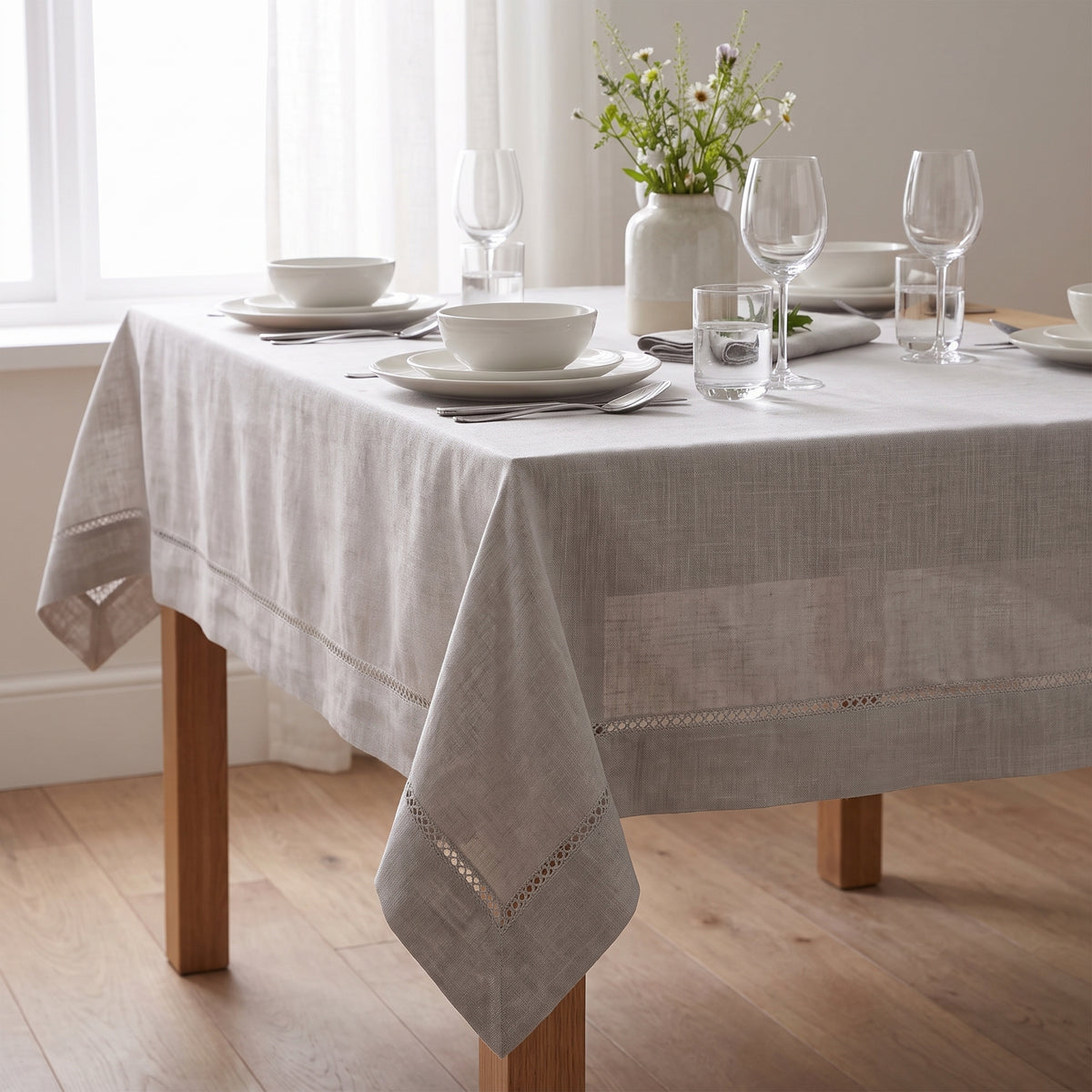 Nappe Florence en polyester texturé avec finition ajourée sur une table dressée avec vaisselle blanche et fleurs